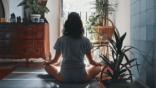Mulher sentada numa sala com várias plantas faz meditação